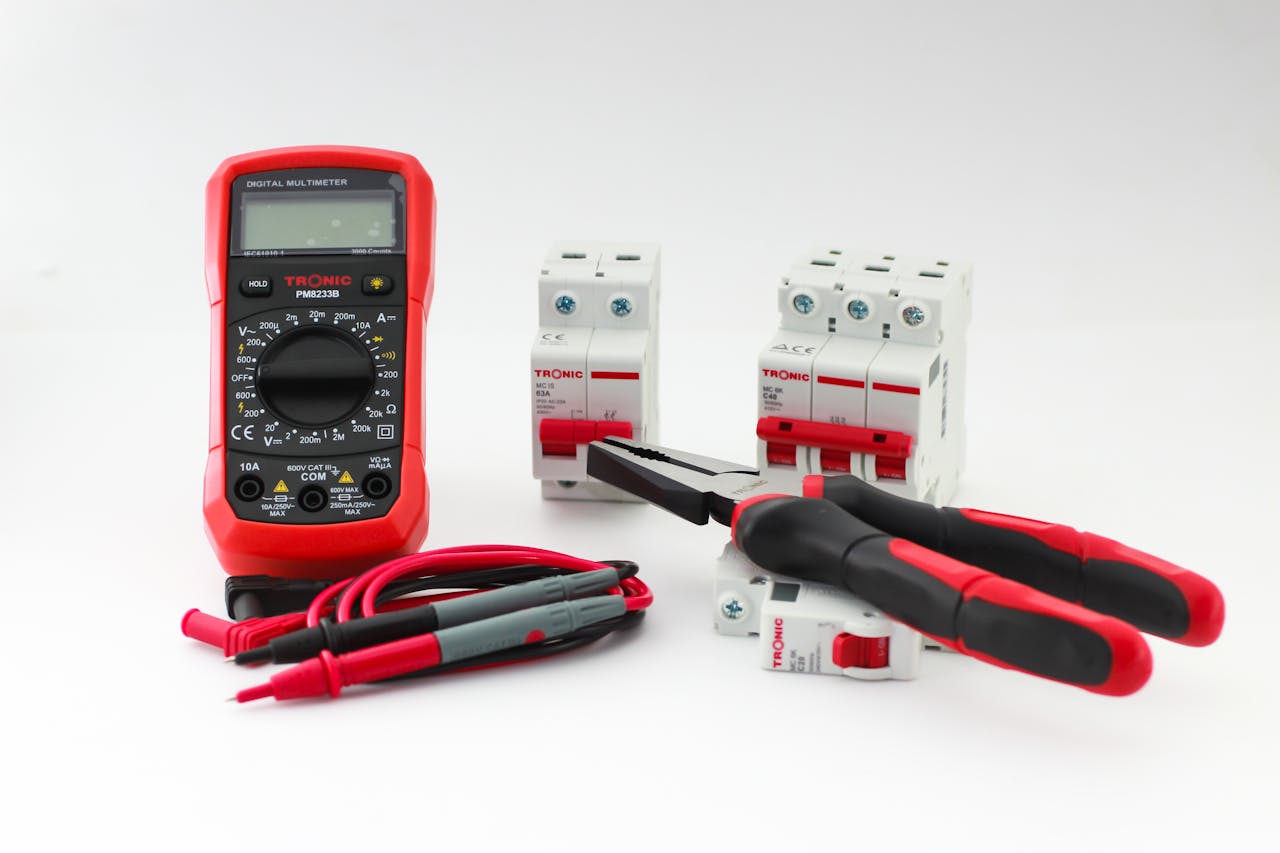 our-journey-03 Close-up of a digital multimeter with electrical tools and circuit breakers on a white background.