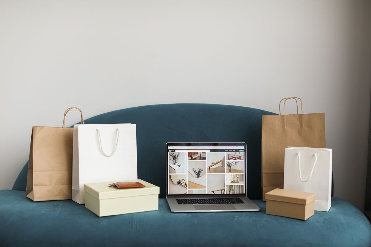 our-journey-01 A laptop surrounded by shopping bags and boxes on a blue sofa, ideal for online shopping themes.